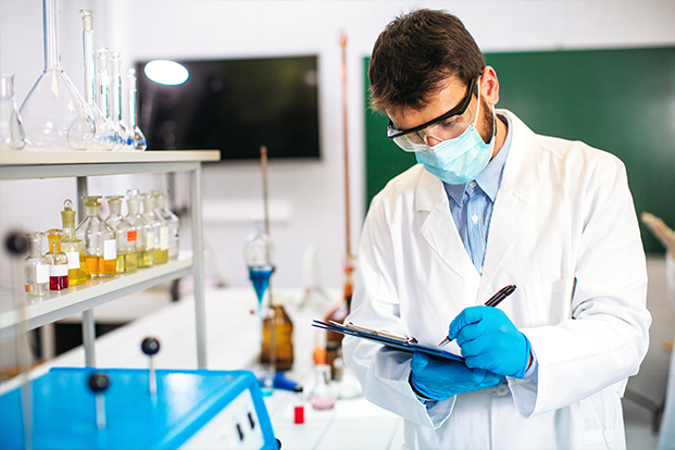 Mann der mit einem Klammbrett in einem Chemielabor etwas kontrolliert Mann der mit einem Klammbrett in einem Chemielabor etwas kontrolliert
