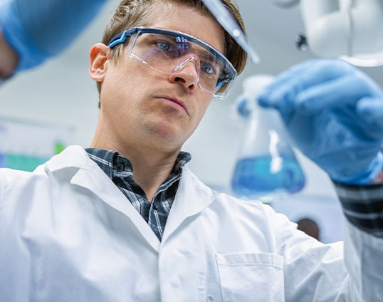 Chemische Analyse und Forschung im Labor Ein Wissenschaftler im Labor analysiert eine Flüssigkeit in einem Erlenmeyerkolben und trägt Schutzbrille, Handschuhe und Laborkittel.