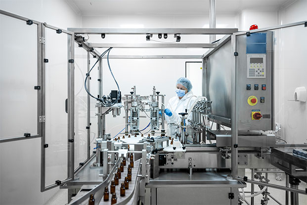 Überwachung der automatisierten Medikamentenabfüllung im Reinraum Person in Schutzkleidung überwacht Abfüllanlage für Medikamentenfläschchen