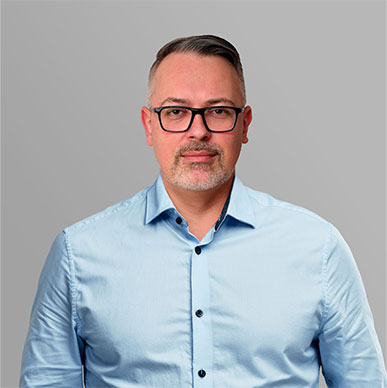 Ihr Ansprechpartner für das Projekt Porträt eines Ansprechpartners mit Brille und blauem Hemd vor grauem Hintergrund