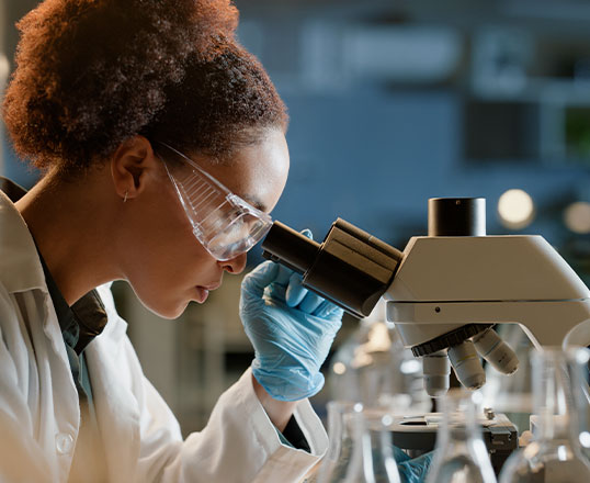 Forschung und Analyse im modernen Labor Wissenschaftlerin im Labor schaut durchs Mikroskop, umgeben von Reagenzgläsern