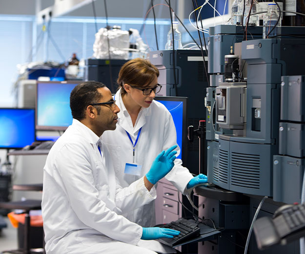 Zwei Chemietechniker bedienen gemeinsam ein Analyseger&auml;t und &uuml;berwachen Messprozesse im Labor.