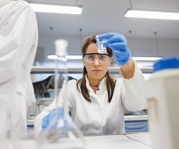 Eine Chemietechnikerin untersucht eine Laborprobe und kontrolliert deren Eigenschaften unter sicheren Arbeitsbedingungen.