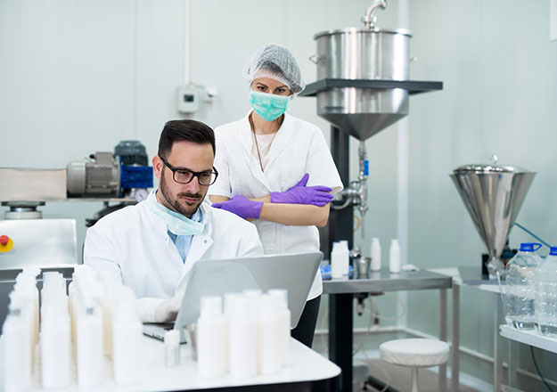 Zwei Fachkr&auml;fte &uuml;berwachen Produktionsprozesse und kontrollieren die Qualit&auml;t in einer pharmazeutischen Fertigungsumgebung.