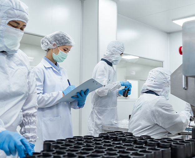 Mehrere Mitarbeitende in Schutzkleidung &uuml;berwachen Produktionsprozesse und dokumentieren Arbeitsschritte in einem Reinraum.