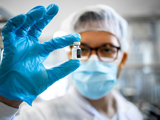 Kontrolle eines Impfstoff-Vials im Labor Laborant mit Schutzkleidung hält ein Fläschchen Impfstoff in die Kamera