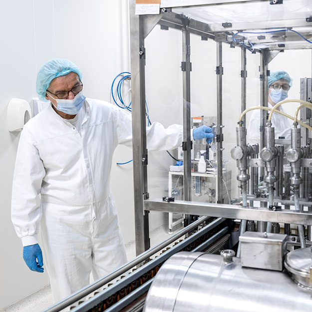 Qualitätskontrolle an einer pharmazeutischen Produktionsanlage Zwei Mitarbeitende in Schutzkleidung überwachen Abfüllanlage im Reinraum