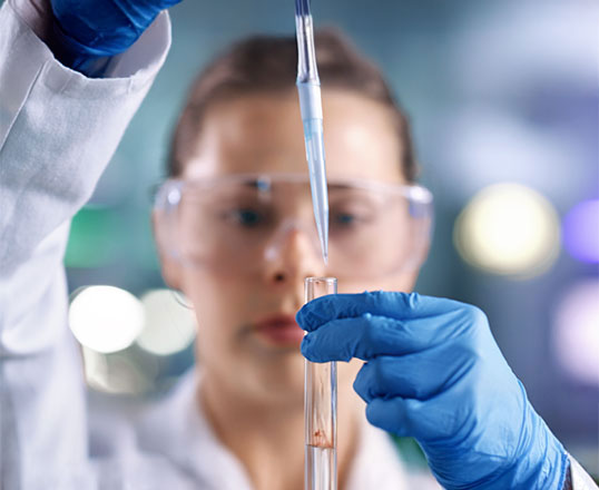 Wissenschaftlerin pipettiert Fl&uuml;ssigkeit ins Reagenzglas mit Schutzkleidung